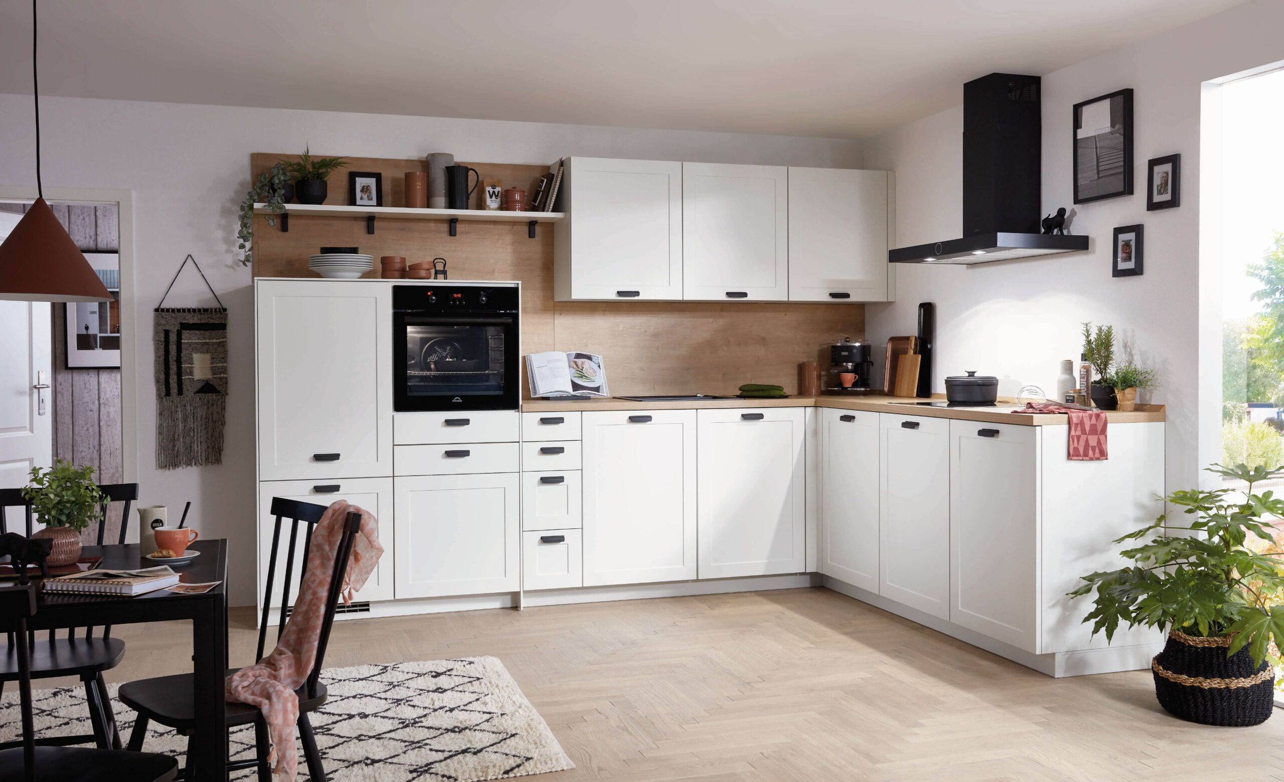 Bright white L-shaped kitchen with wood accents, black appliances, a patterned rug, and a black dining table.
