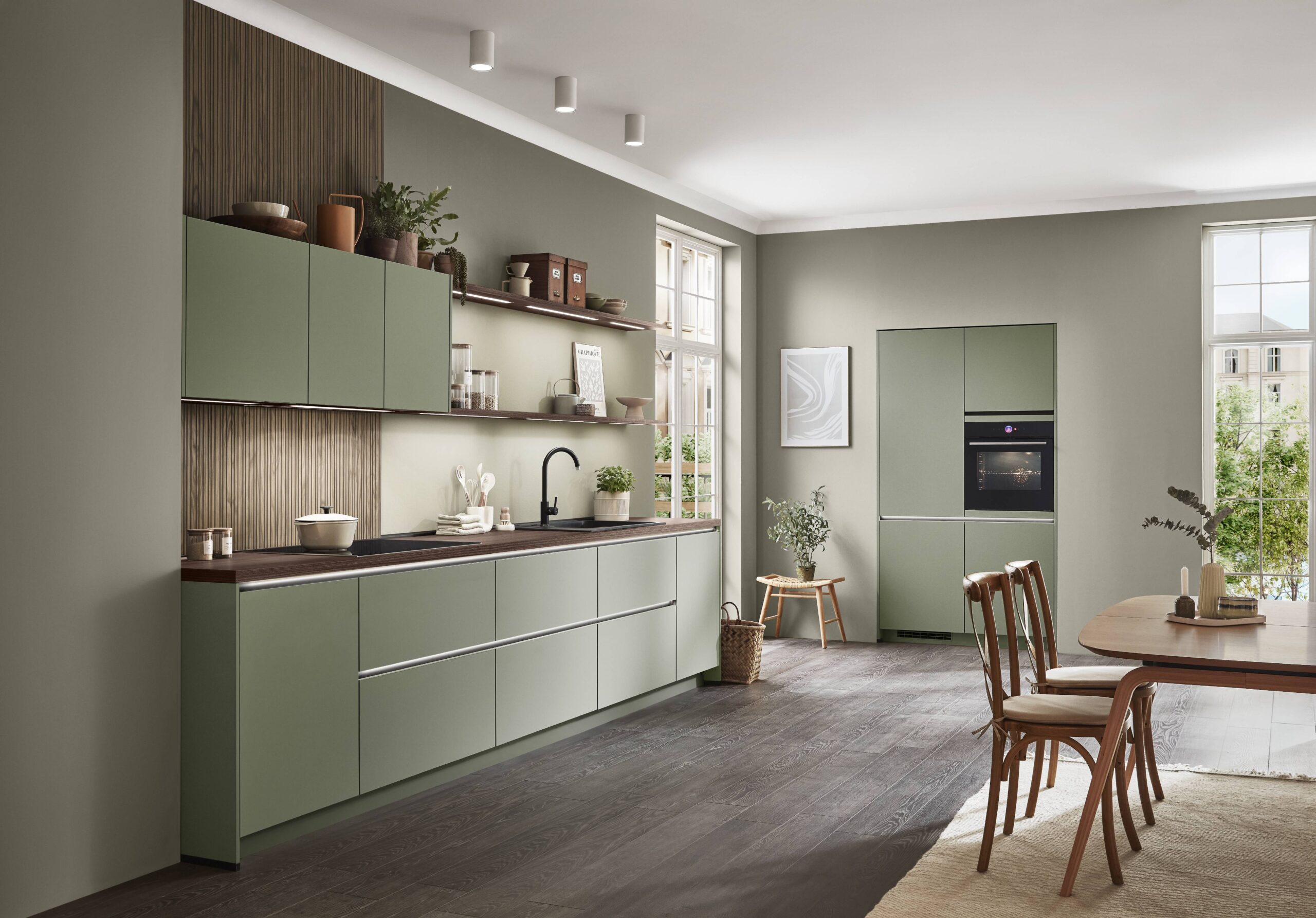 Stylish green kitchen with dark wood accents, including countertops, open shelving, and a wood slat backsplash. A light wood dining table with chairs is also visible.
