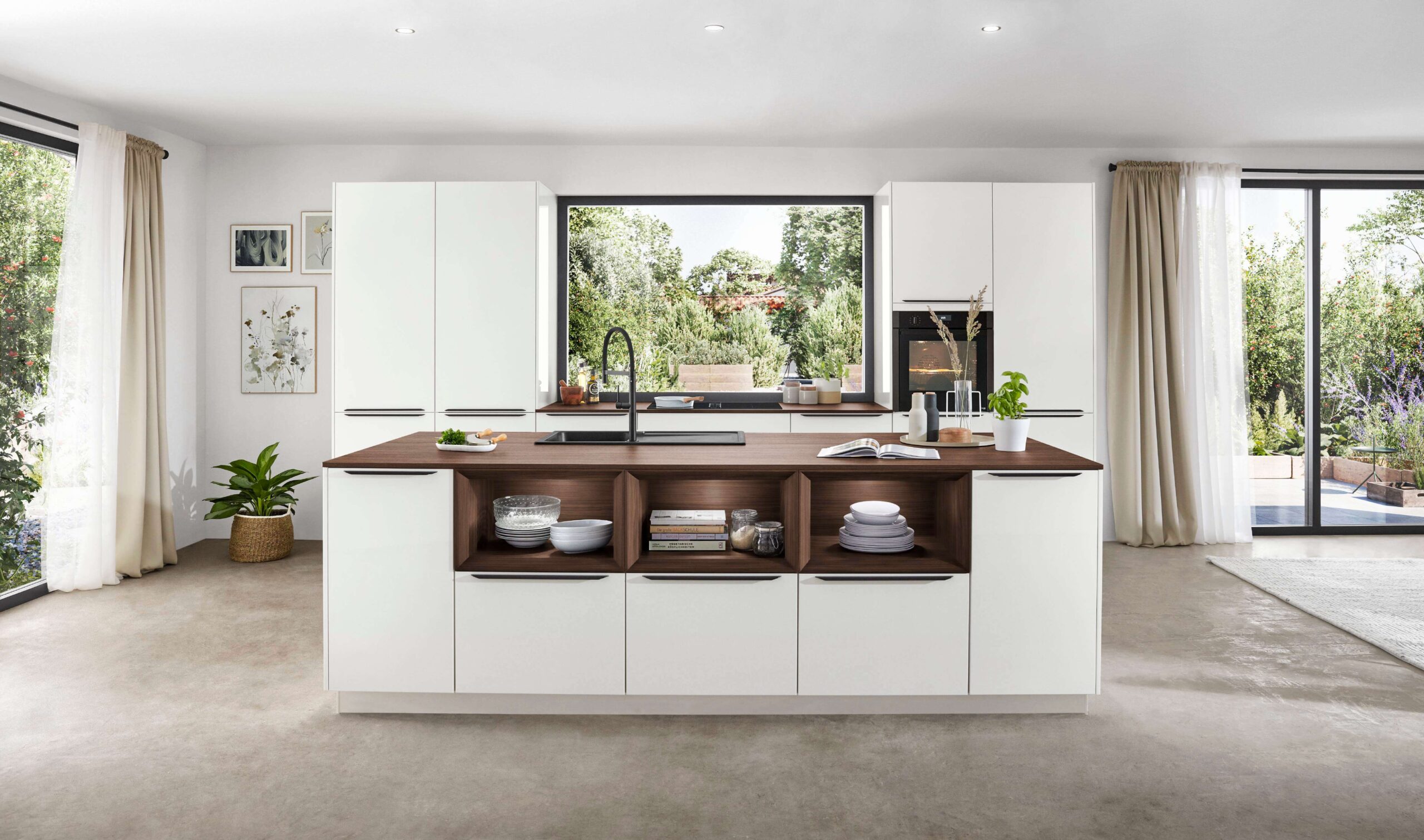 Minimalist white kitchen with a dark wood countertop island featuring open shelving. Large windows and white curtains brighten the space.