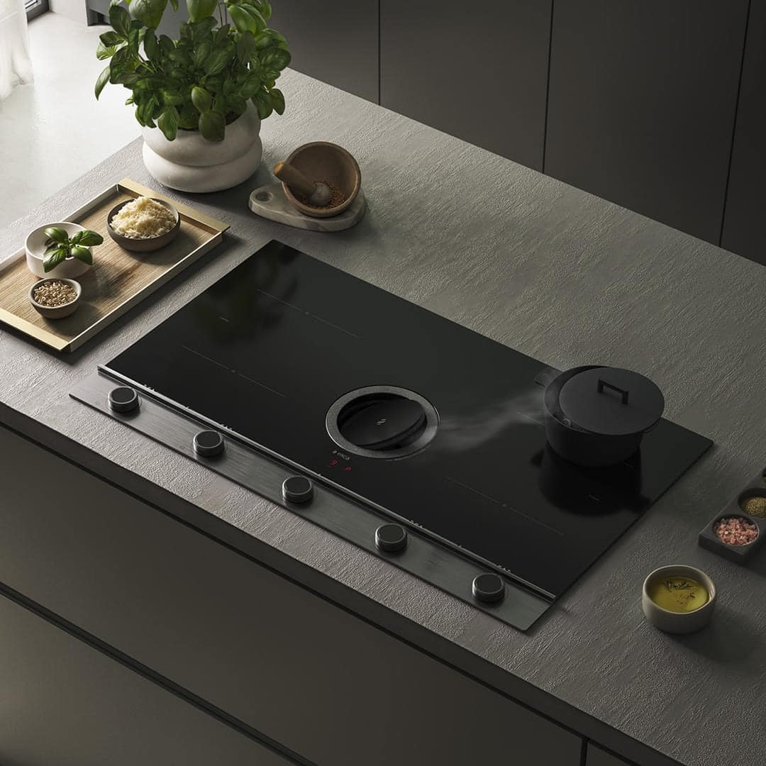 Black Elica induction cooktop with a built-in downdraft vent on a gray countertop. A pot with a lid is steaming on the cooktop.