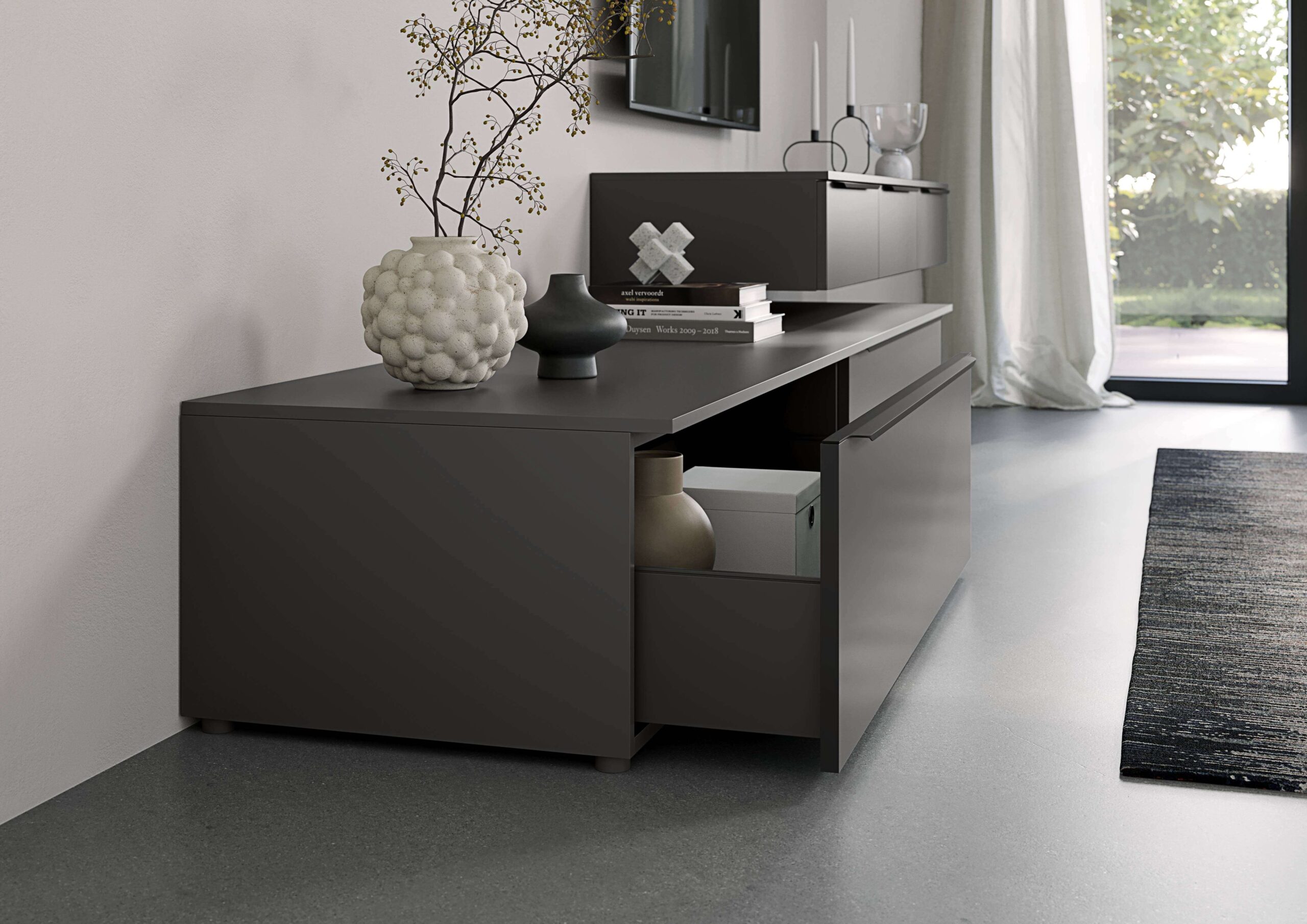 Dark gray media console with an open drawer. Decorative objects and books are placed on top, with a rug and window in the background.