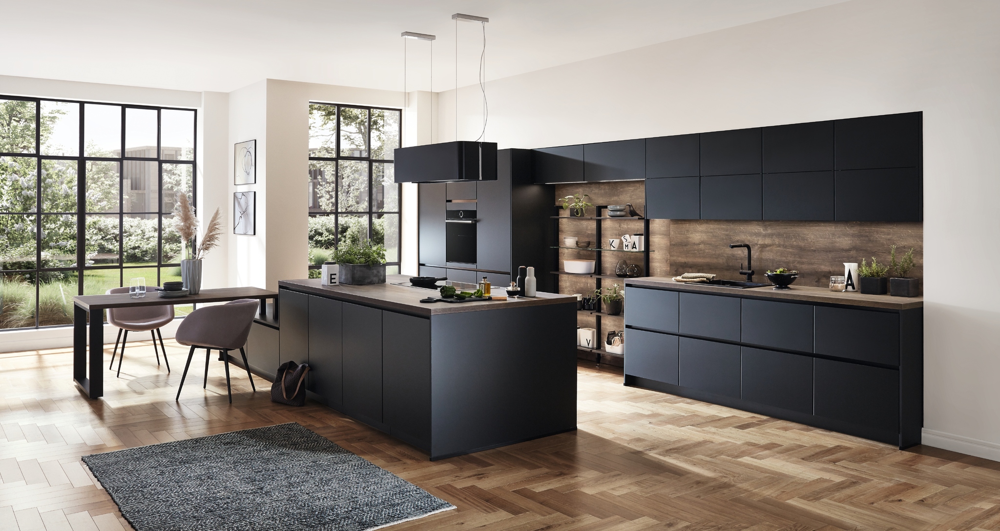 A modern, all-black kitchen with a spacious island and dark wood accents. Large windows provide natural light.