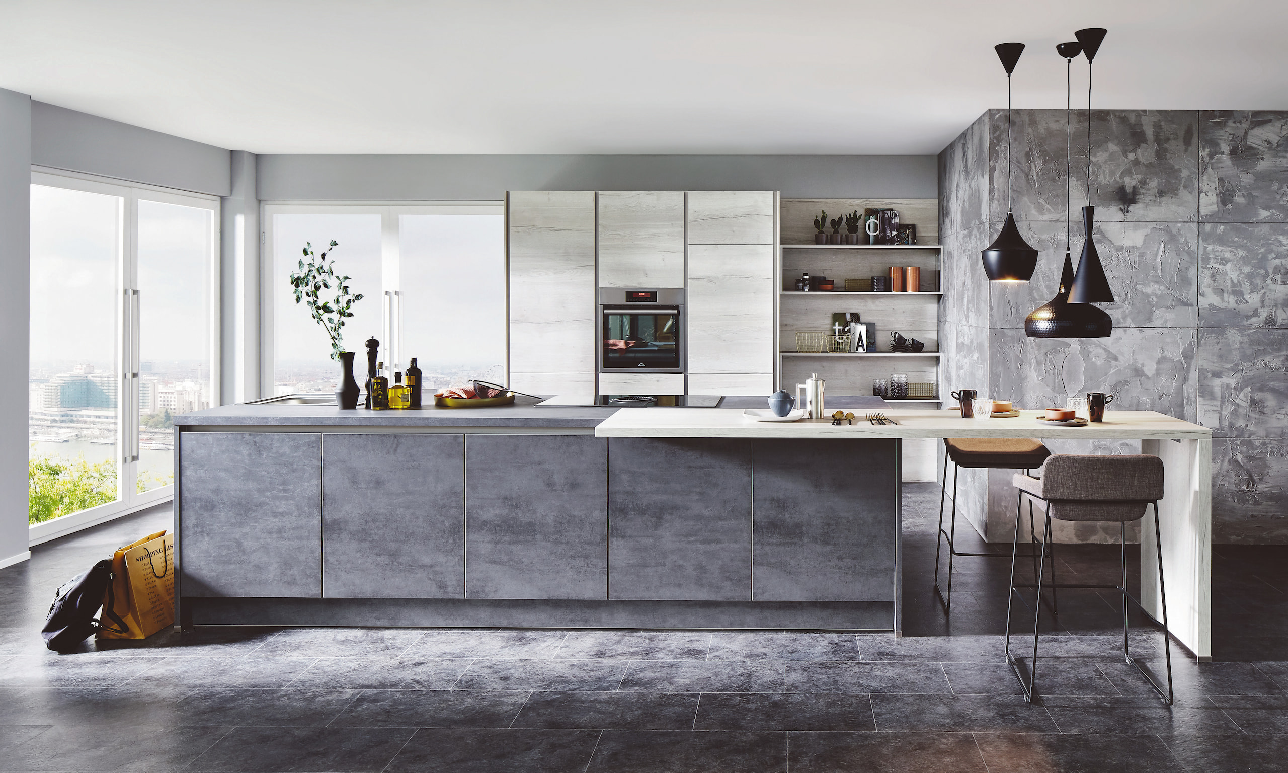 Modern kitchen with a large gray island, a breakfast bar, and pendant lights. Large windows offer a panoramic view.