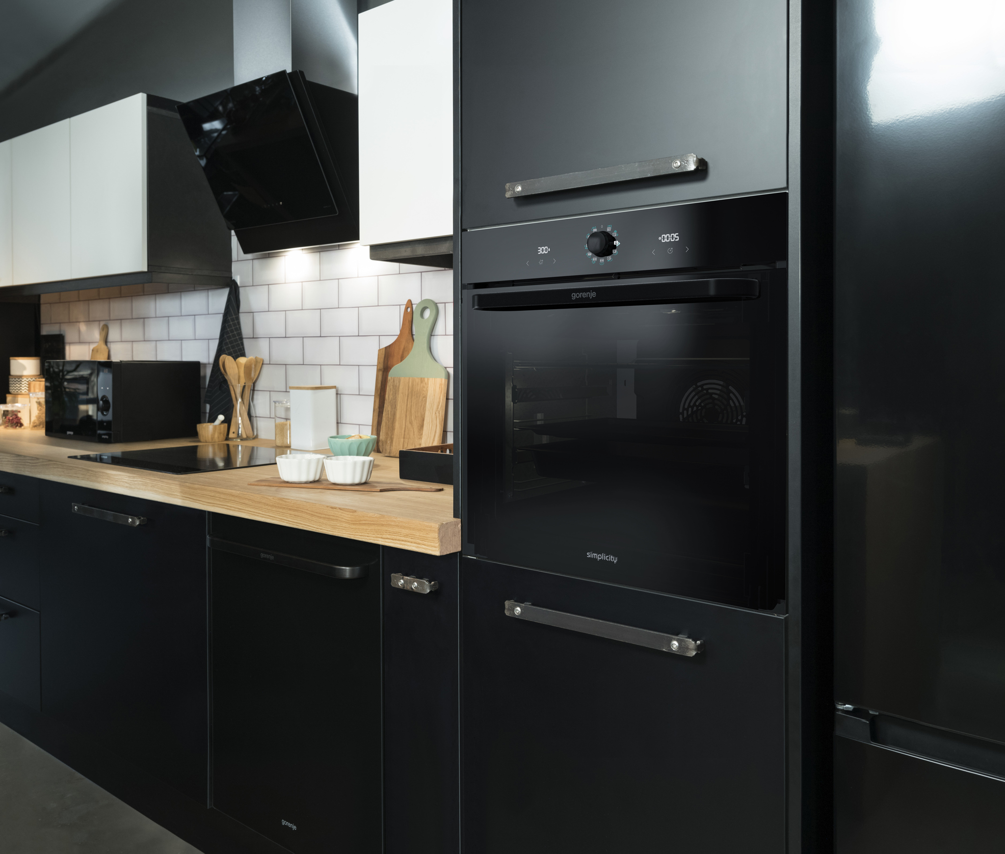 Modern black kitchen with stainless steel handles and a built-in black Gorenje oven.