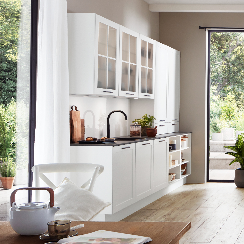 White kitchen with glass-front cabinets, a dark countertop, and an open view to the outside.