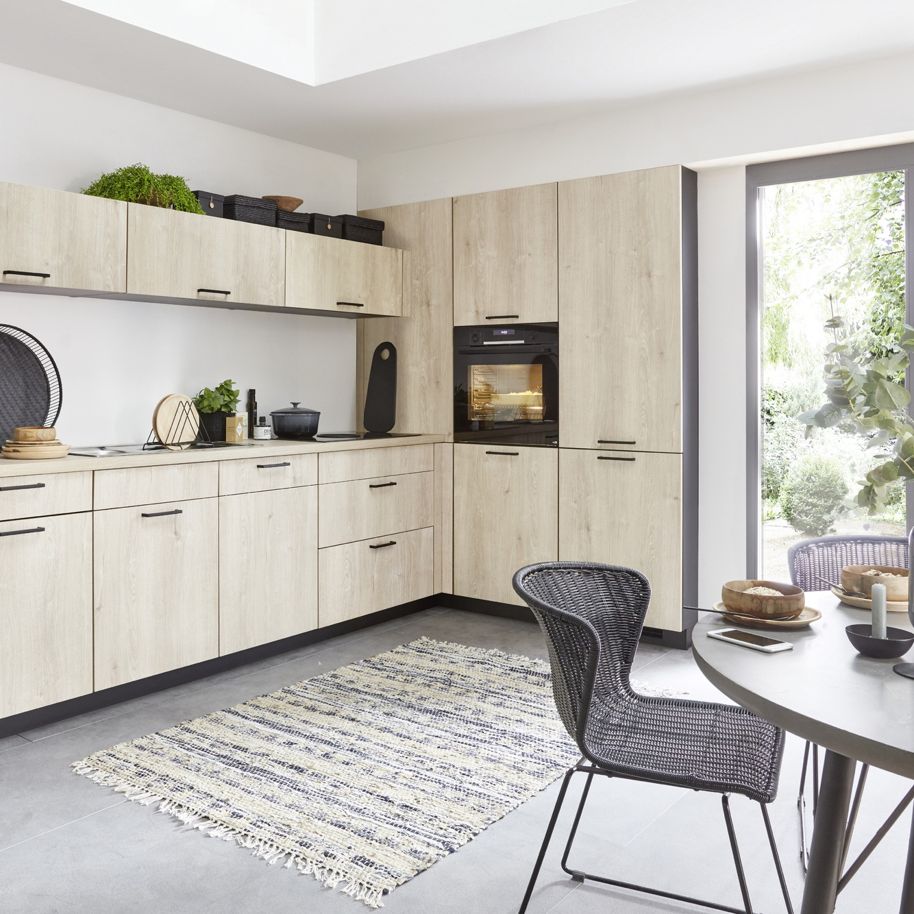 Light wood kitchen with black appliances, a patterned rug, and a dining table.