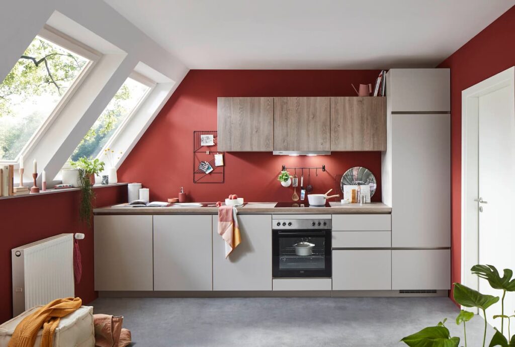 A bold red modern kitchen with slanted windows and wooden cabinetry, demonstrating a fresh take on modern kitchen interior design in a cozy attic space.