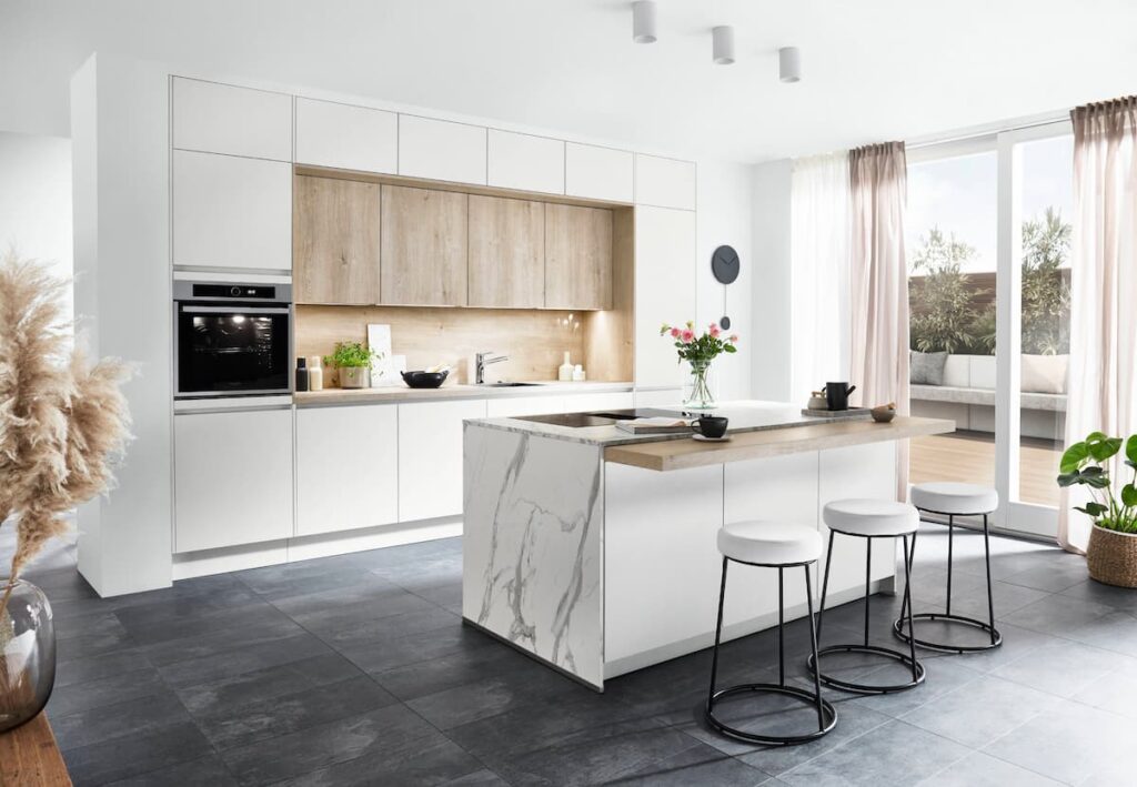 A bright kitchen with a marble island, light cabinetry, and black slate flooring, showcasing one of the best high-traffic flooring materials for kitchens.