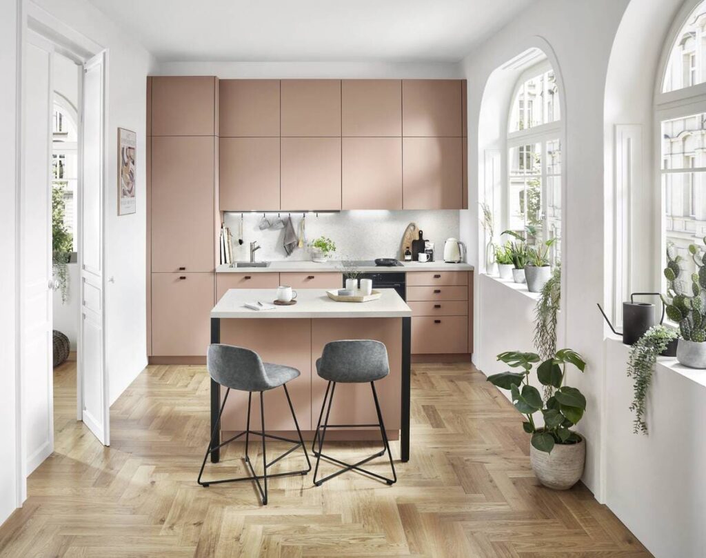 Chic pink kitchen in Bangkok with modern fixtures and large windows, offering warmth and light.