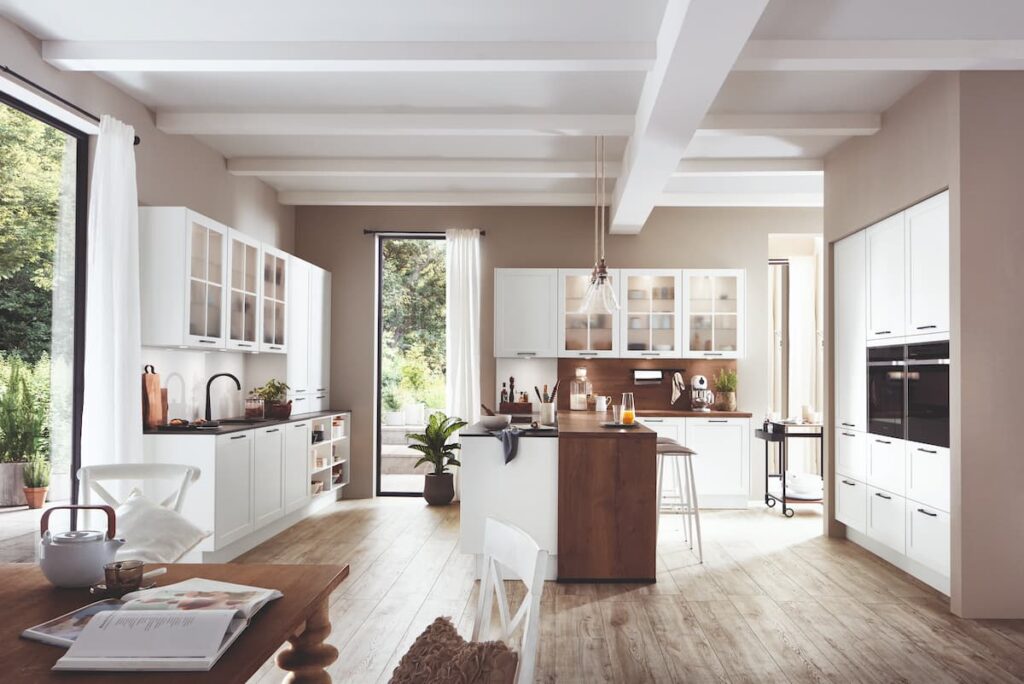 Classic white kitchen with light wood flooring, featuring exposed ceiling beams and a cozy dining area, illustrating the best kitchen flooring material for a warm and inviting space.