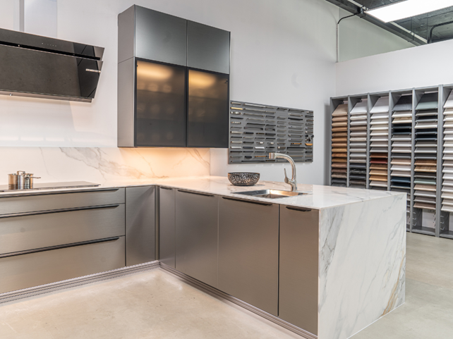 A modern gray kitchen display in a German kitchen showroom, featuring sleek cabinetry, marble countertops, and integrated appliances.