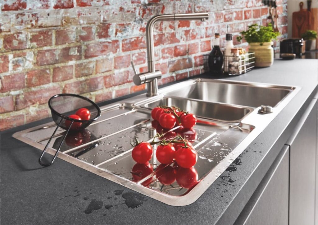 A stainless-steel kitchen sink with a brick backsplash. Consider the cost of individual elements when planning how much to spend on a kitchen renovation.