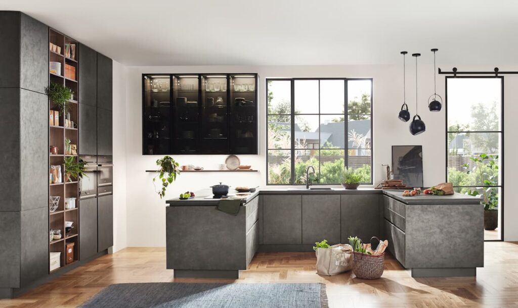 Modern industrial kitchen with dark gray cabinets, large windows, and wooden herringbone flooring, showcasing innovative kitchen interior design ideas.