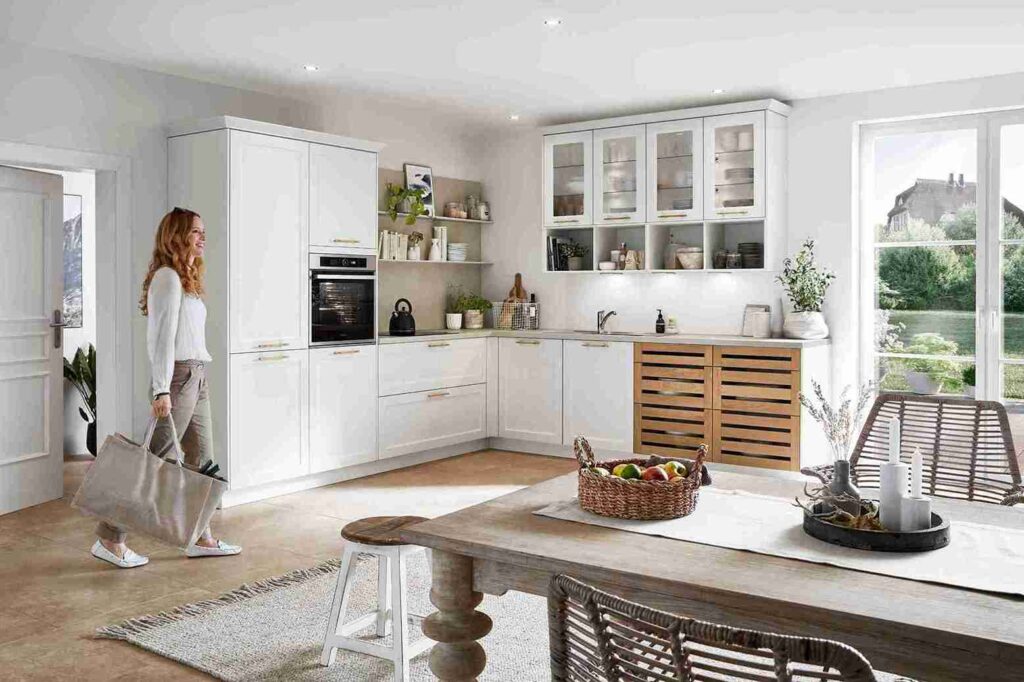 A bright and airy white kitchen designed by a modern kitchen company, featuring wood accents, glass-front cabinets, and a welcoming dining area.