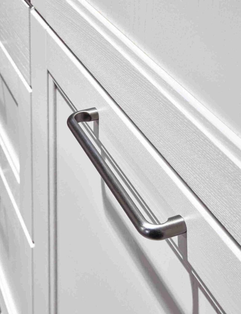 Close-up of a brushed metal handle on a white cabinet door, showcasing the attention to detail offered by a modern kitchen company.