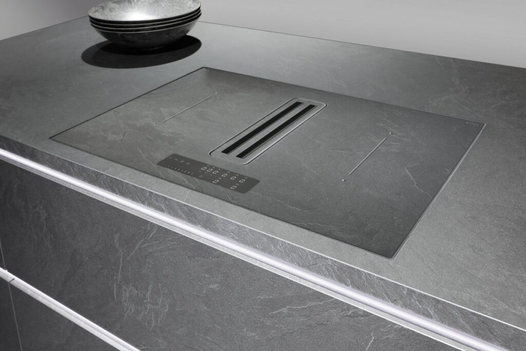A high-end German kitchen featuring a sleek, integrated cooktop on a dark grey countertop.