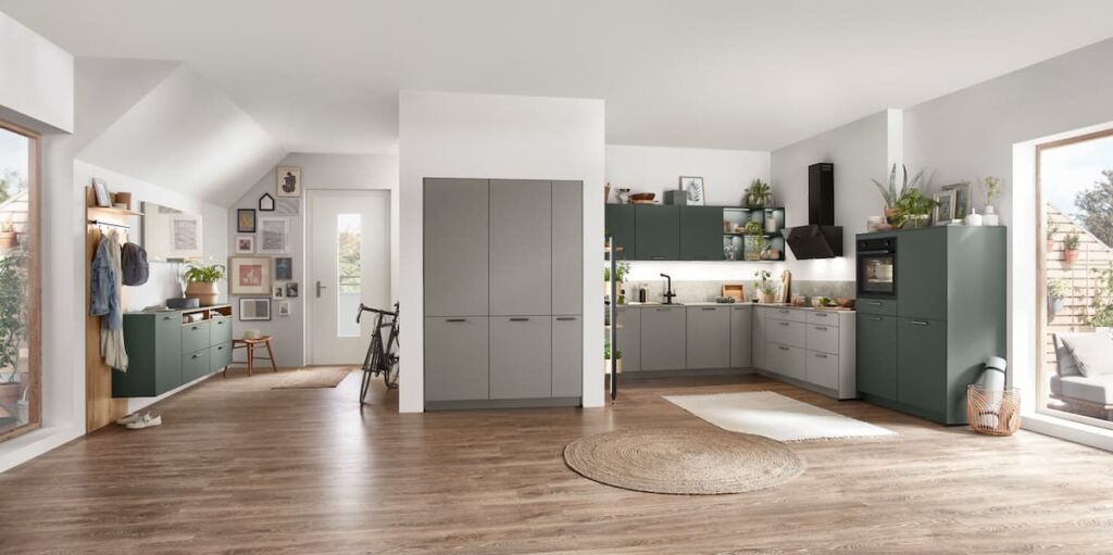 ครัวที่มีการจัดวางอย่างกว้างขวางด้วยตู้สีเขียวด้านด้าน และตู้สีเทา ผสมผสานสไตล์โมเดิร์นกับแสงธรรมชาติ สร้างบรรยากาศที่เปิดโล่งและอบอุ่นด้วยโทนสีธรรมชาติและการตกแต่งที่สบายตา
