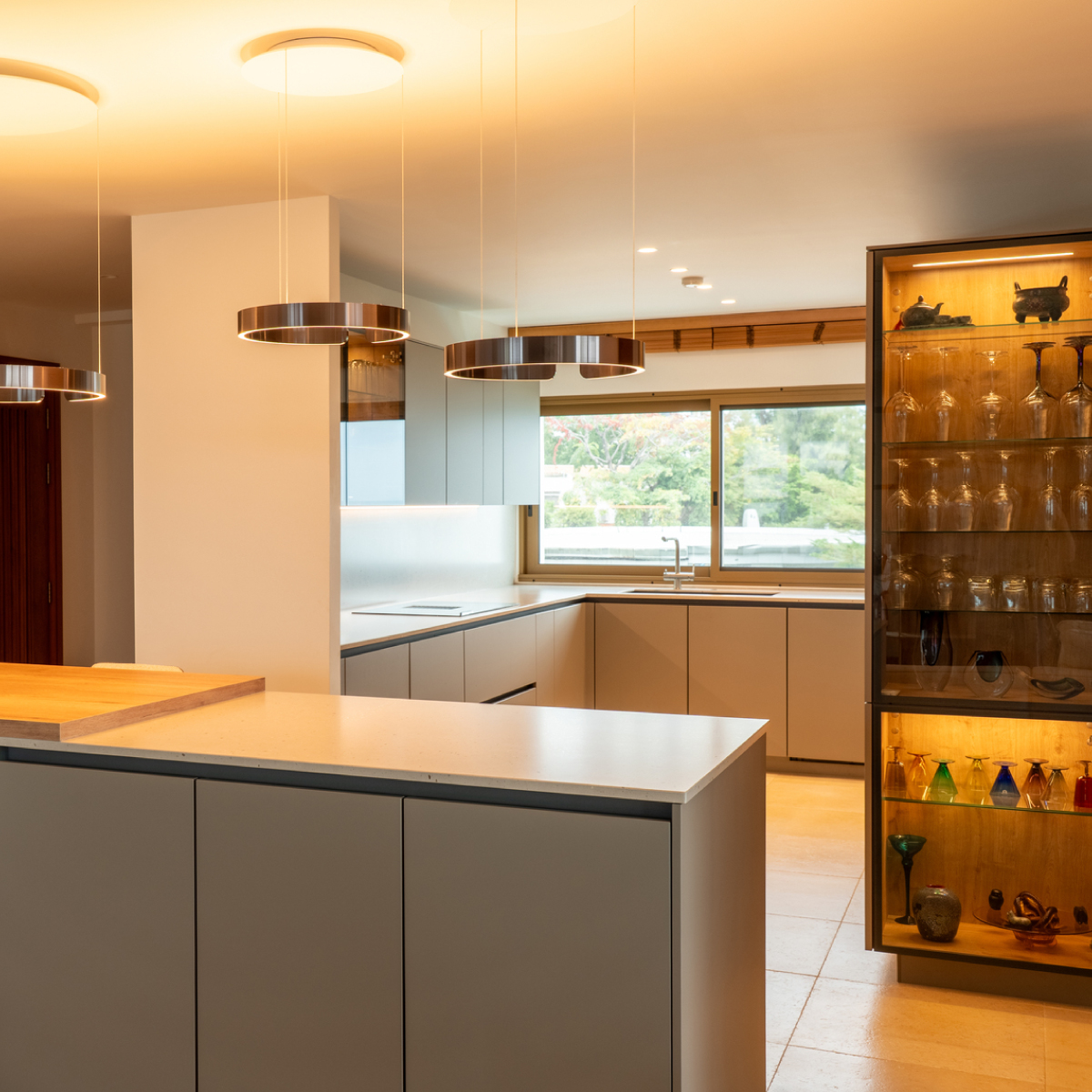 Modern kitchen with an island, circular pendant lights, and a glass-fronted cabinet.