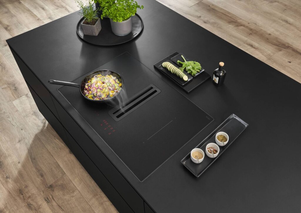 Modern kitchen island in matte black featuring a built-in downdraft extractor and a clean, minimalist cooking setup.