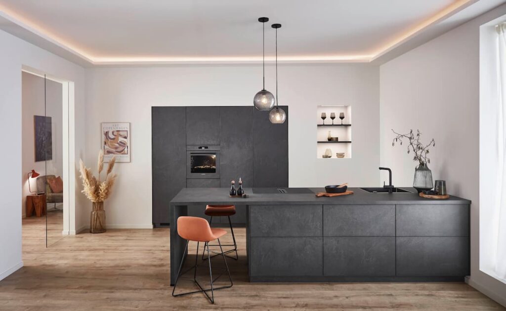 A sophisticated modern kitchen featuring dark stone-effect cabinetry, a central island with bar seating, and an illuminated wall niche for curated display.
