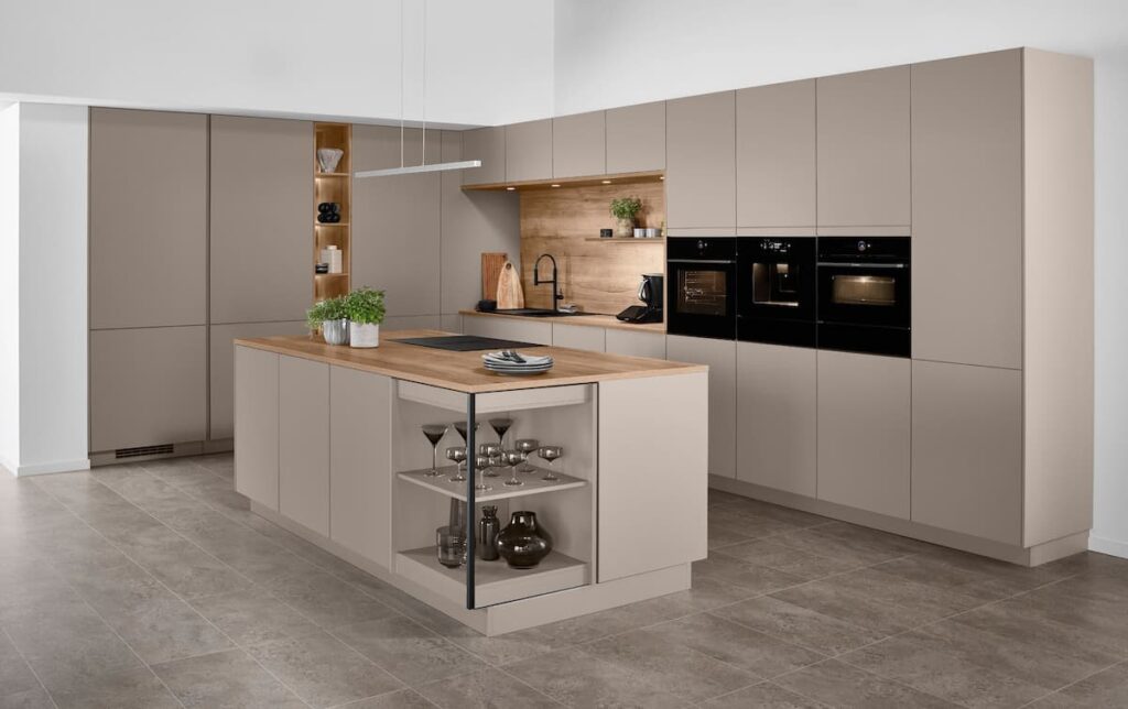 A U-shaped modern kitchen blending taupe matte fronts with a warm wood backsplash niche and a functional island featuring our all-new FurnSpin rotating cabinet.