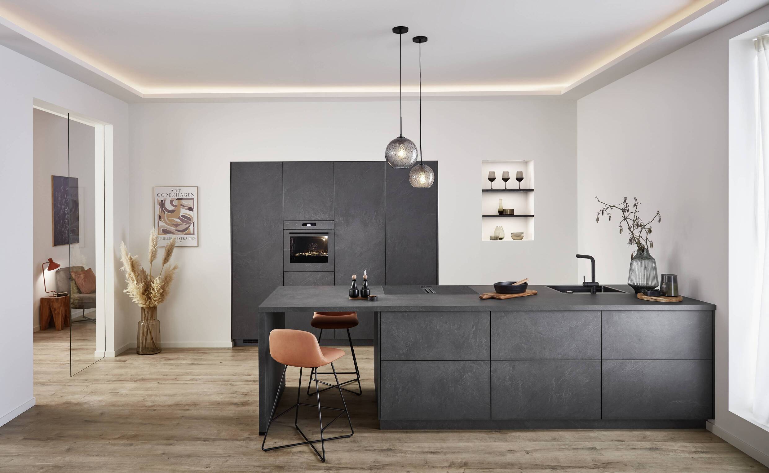 A sophisticated minimal kitchen featuring a textured dark matte island with handleless cabinetry and pendant lighting, showcasing clean lines and high-end material finishes.