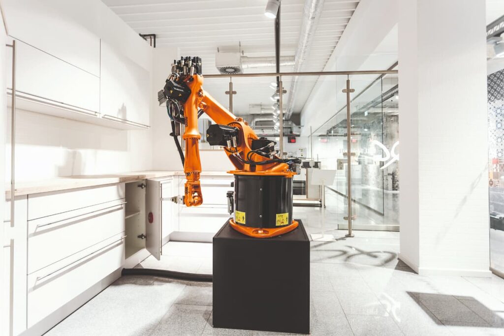An industrial robotic arm performing precision tasks, highlighting the difference between factory-engineered modular systems and traditional built in kitchen carpentry.