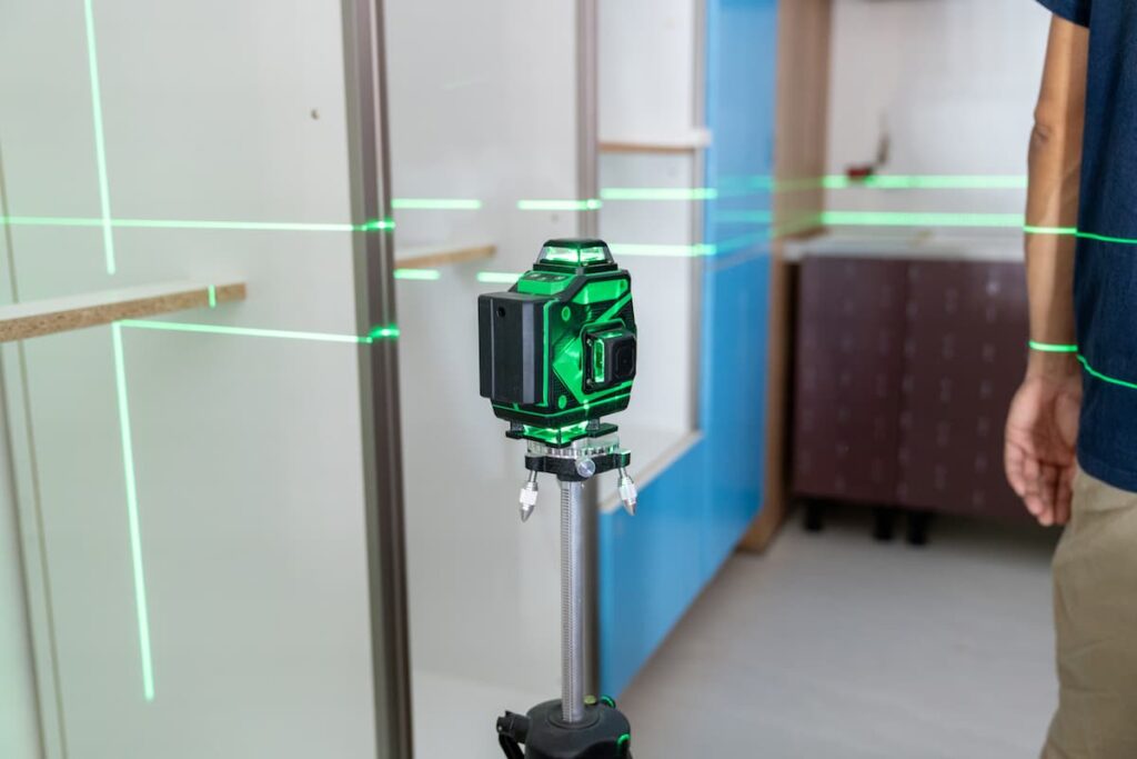 A construction professional using a green laser level to ensure perfect alignment during the installation of a modular built in kitchen.