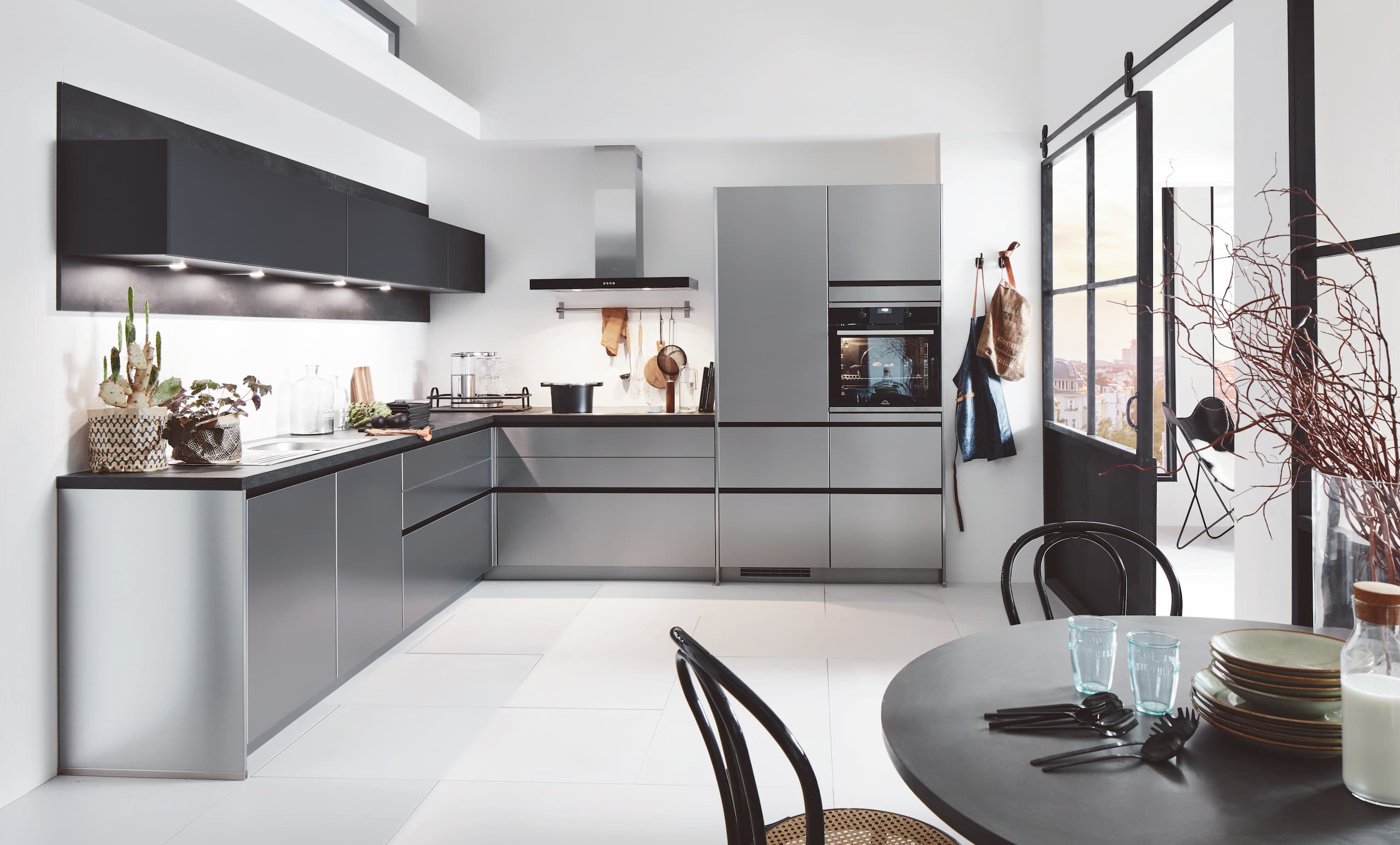 A minimalist handleless German kitchen featuring sleek stainless steel reproduction cabinetry with dark horizontal recessed profiles, a contrast black countertop, and matching matte black overhead cabinets with integrated LED task lighting.