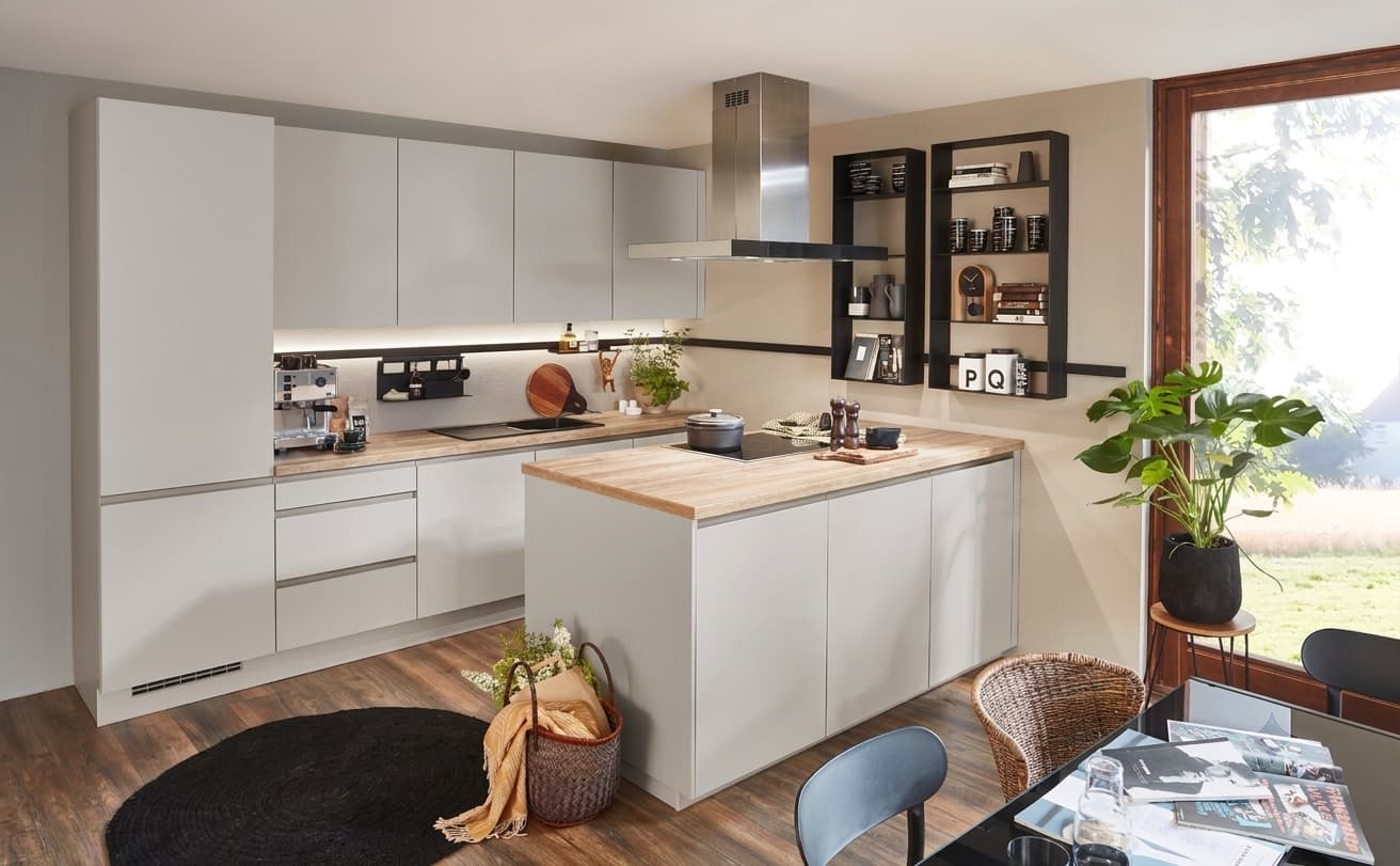 A minimalist handleless German kitchen featuring smooth sand matte cabinetry from the LINE N system, beautifully paired with a light natural wood-grain worktop and matching central island, accented by open black metal display shelves and integrated under-cabinet lighting.