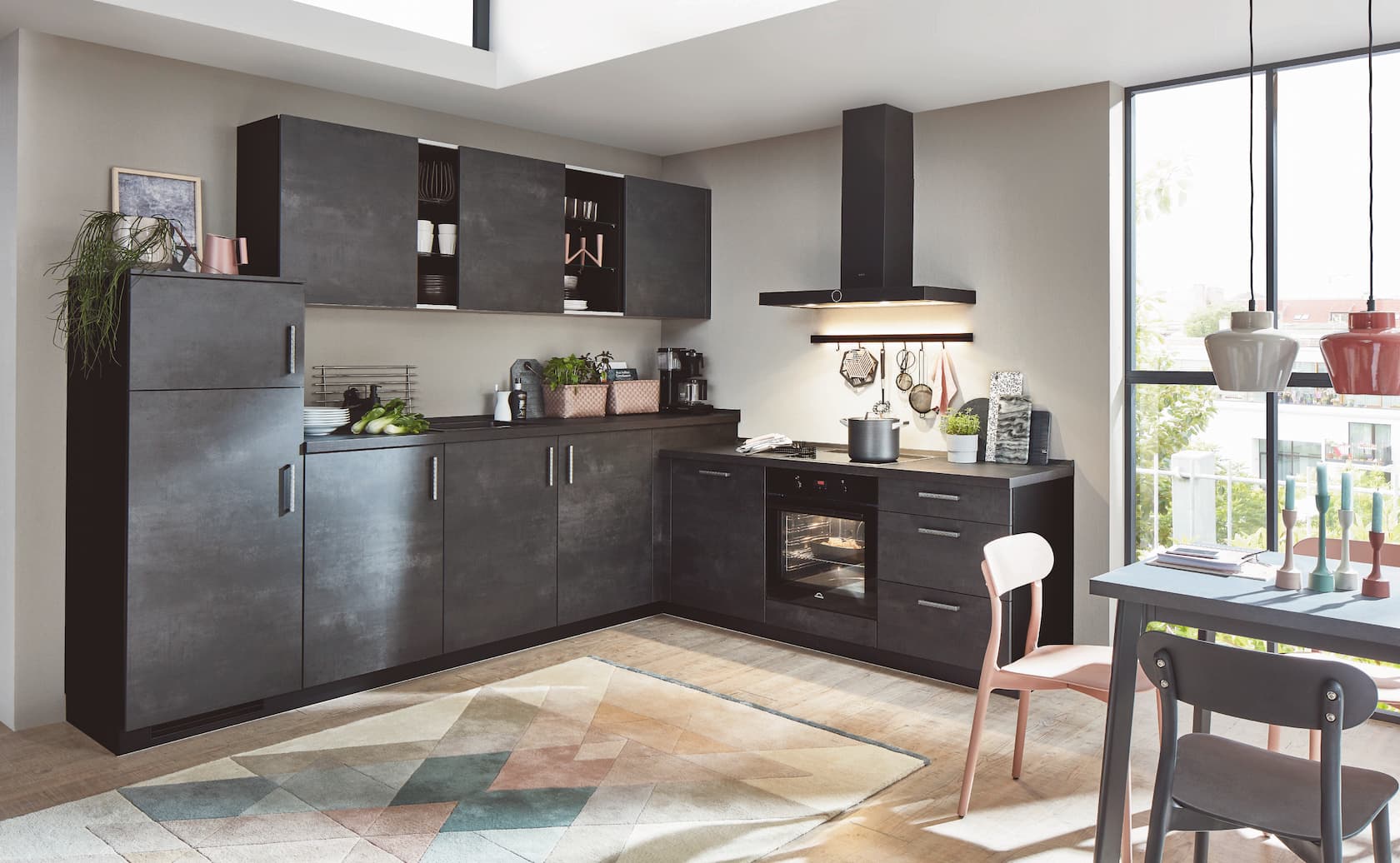 A modern L-shaped industrial-style German kitchen featuring textured steel grey concrete-look cabinetry with vertical and horizontal metal bar handles, a matching dark countertop, a sleek black extractor hood, and a built-in black oven.