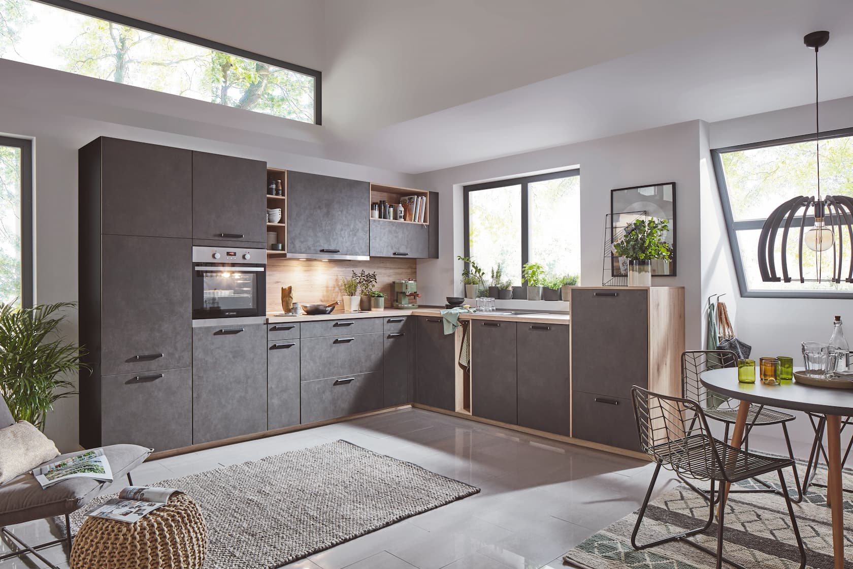 A modern L-shaped German kitchen featuring textured concrete-look grey cabinetry with sleek dark horizontal handles, balanced by warm light wood framing, a matching wooden backsplash, and integrated open wooden shelving units.