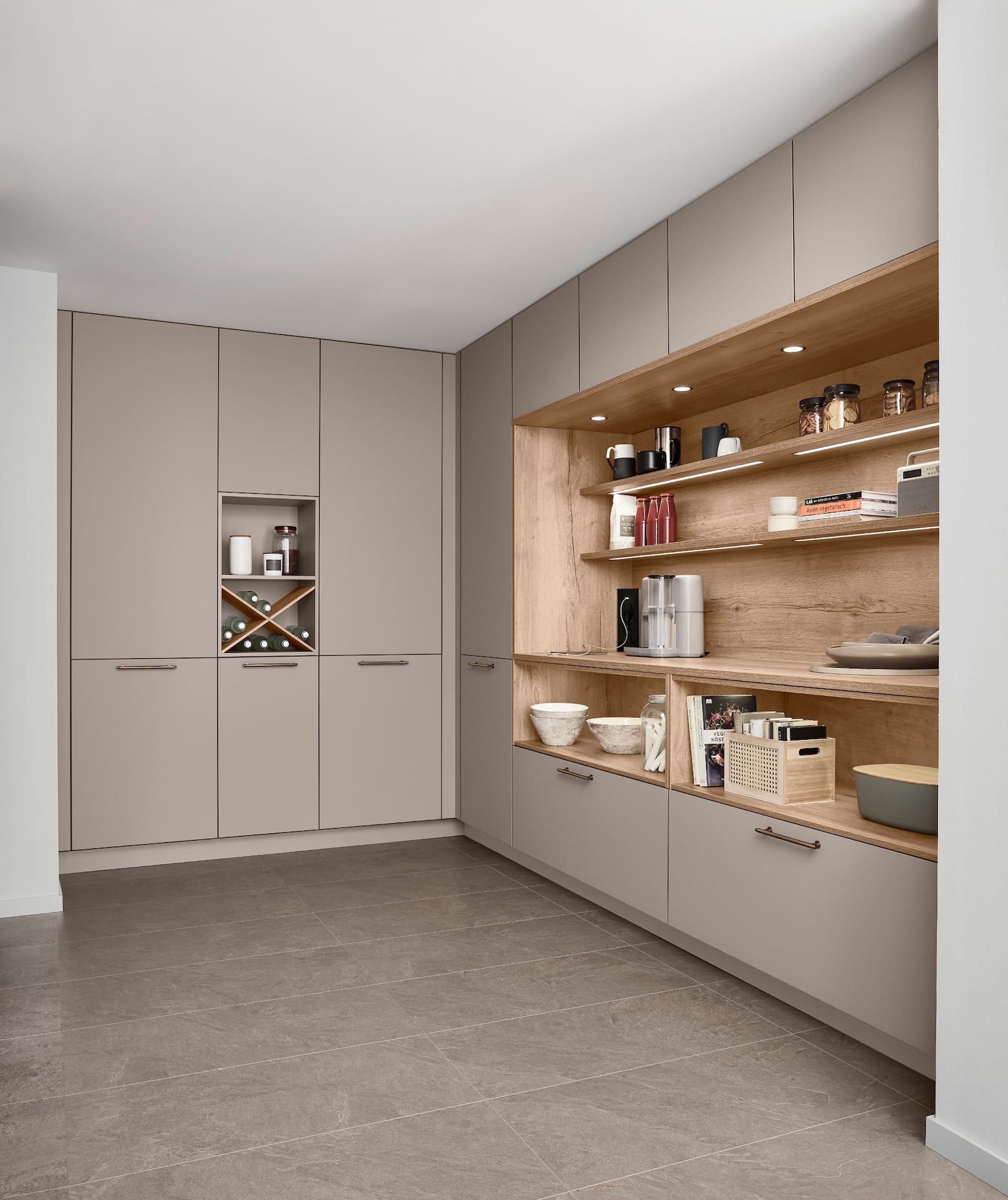 A contemporary floor-to-ceiling German kitchen concept featuring sleek Macchiato Premium matte cabinets with subtle integrated handles, built around a large illuminated Sierra oak reproduction pantry recess with light wood floating shelves and warm accent lighting.