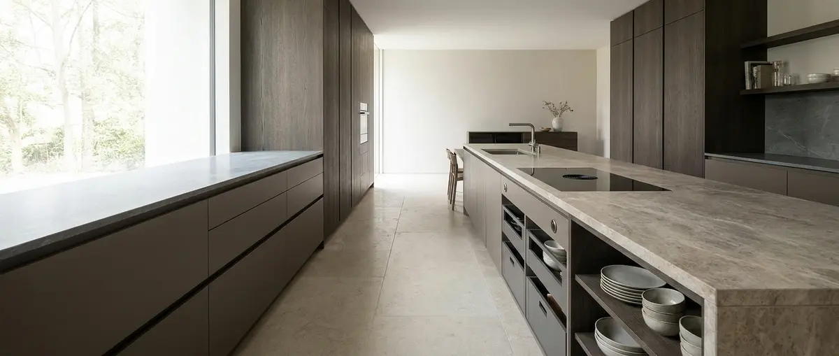 High-end editorial photography of a completed luxury German-style kitchen in a modern Bangkok penthouse. A sophisticated, relaxed Thai homeowner is elegantly pouring morning coffee, enjoying the restful and uncluttered atmosphere of the completed space. Warm natural daylight streams through large windows, highlighting smooth premium surfaces and clean architecture. Focus: A wide-angle, hyper-realistic photograph capturing a high-end German kitchen, strictly adhering to nobilia's signature photography aesthetic. Ratio: wide angle. Lighting: Diffuse natural daylight, soft, even, bright. Camera: Wide-angle lens (16-24mm), full-frame DSLR, crisp focus. Composition: Rule of thirds, strong geometric lines, spacious. NO text, logos, or branding on any surfaces, appliances, or products. NO floating, exploded or disassembled elements. All kitchen components must be fully assembled and grounded.